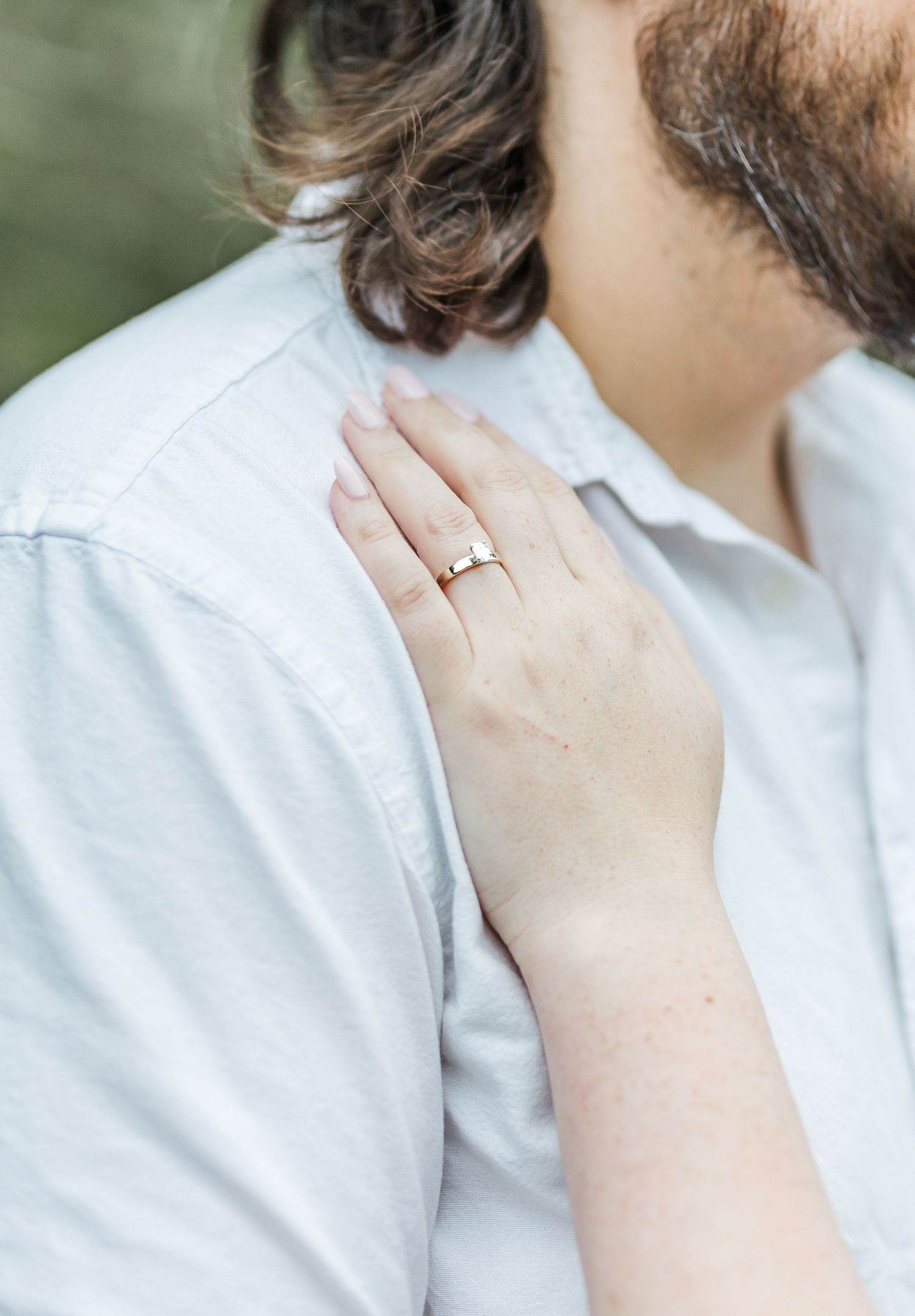 Close-up of engagement ring as hand rests on shoulder in white shirt.