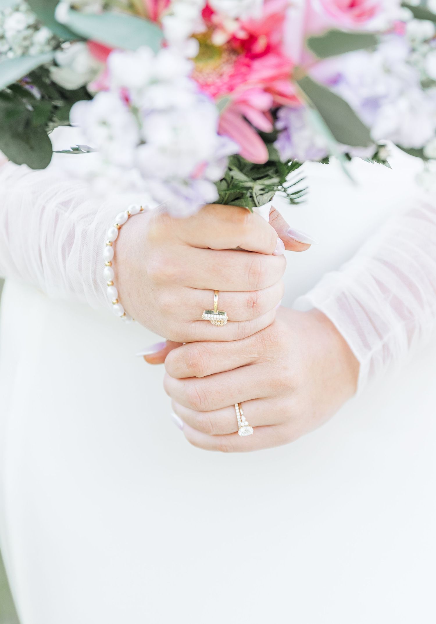 Close-up of bride's hands holding bouquet, showing engagement ring and wedding band.
