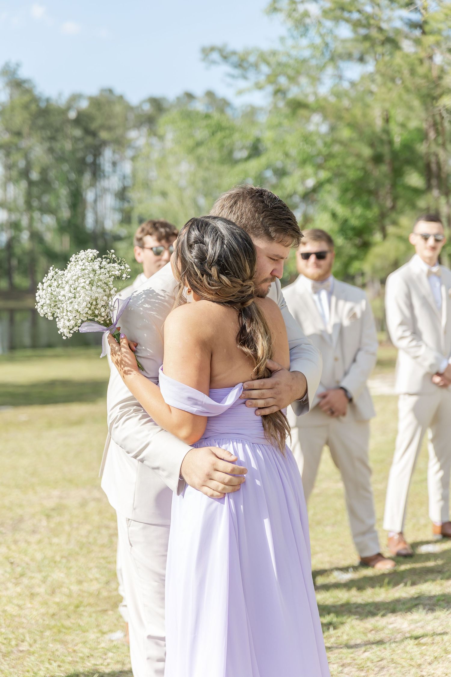 Wedding couple embraces during outdoor ceremony while wedding party watches.