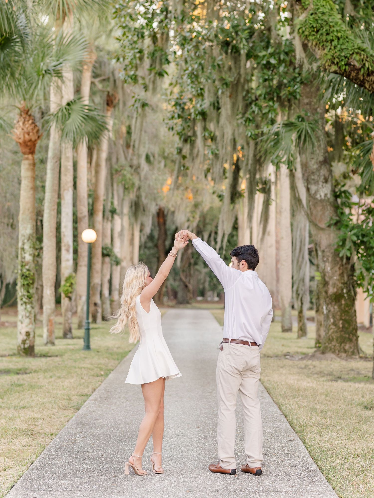 Couple in white dancing on a tree-lined path surrounded by lush tropical greenery.