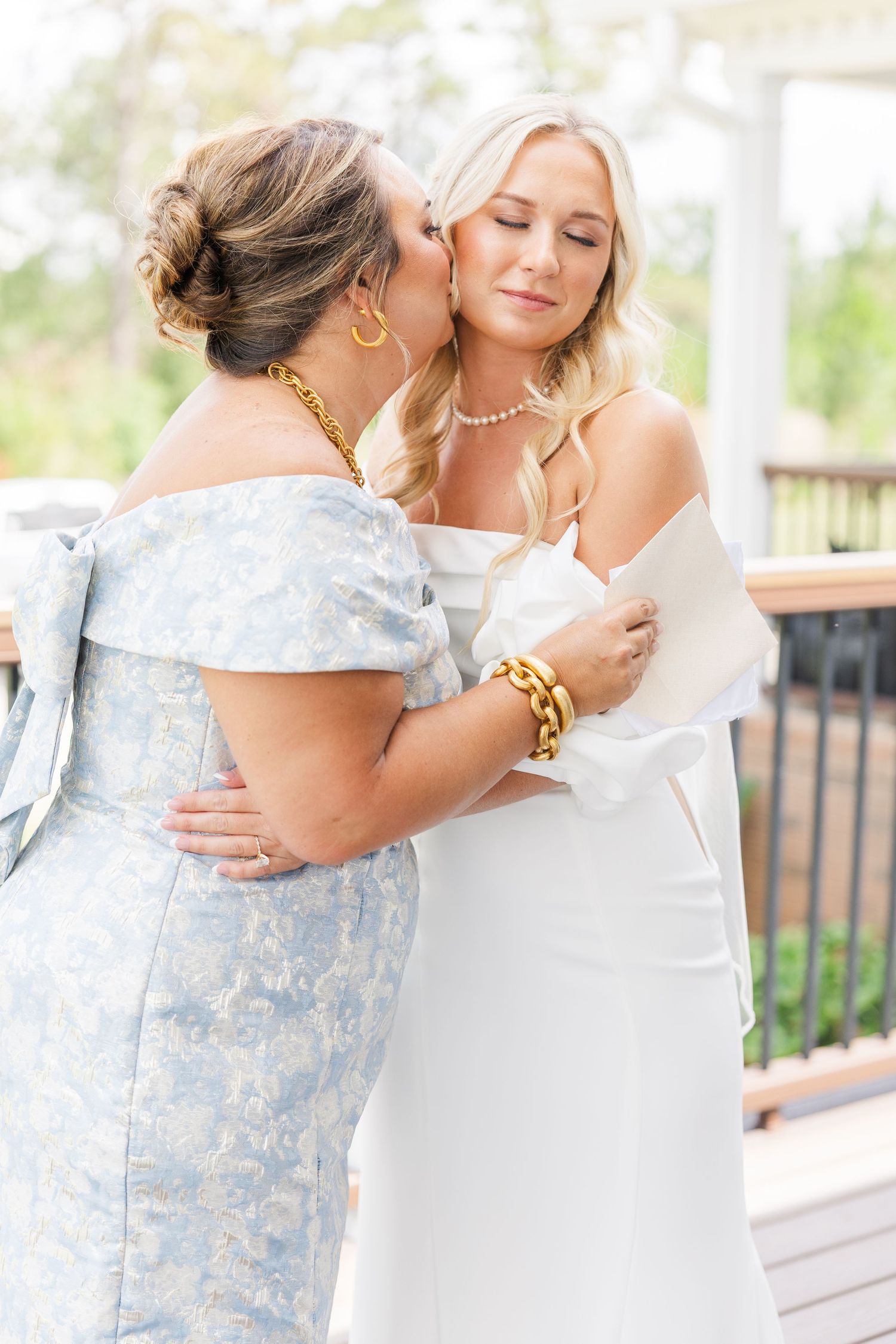 A mother kisses her daughter on the cheek as the bride prepares in her white wedding gown.
