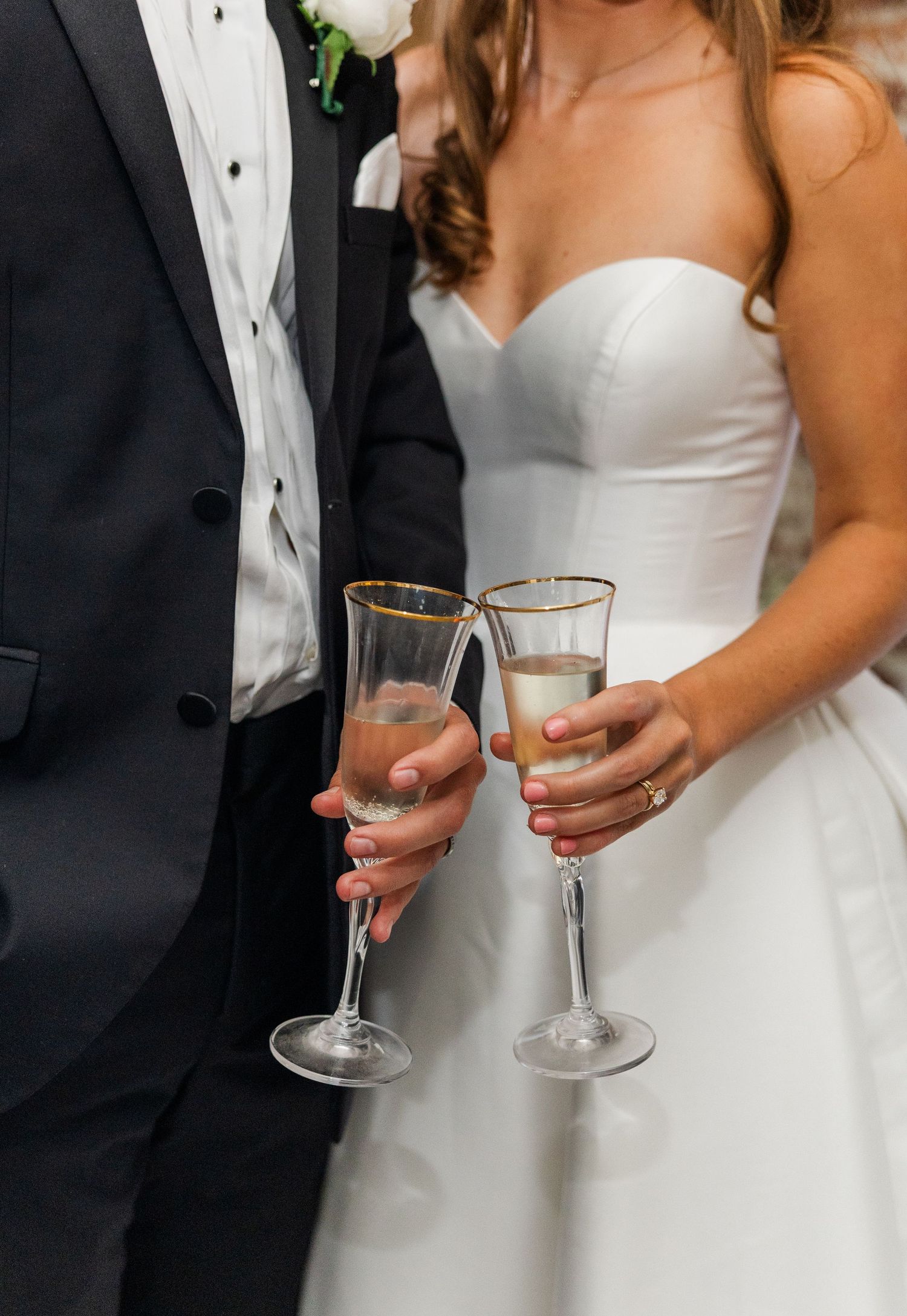 Bride and groom clink gold-rimmed champagne flutes in a wedding reception toast.