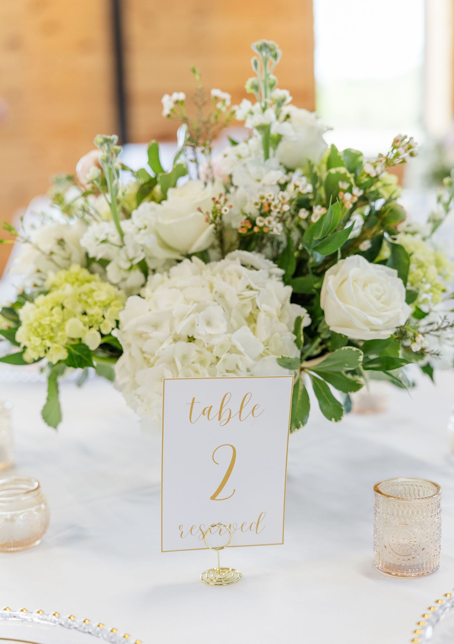 White hydrangea and rose wedding centerpiece with a gold Table 2 reserved sign on a white tablecloth.