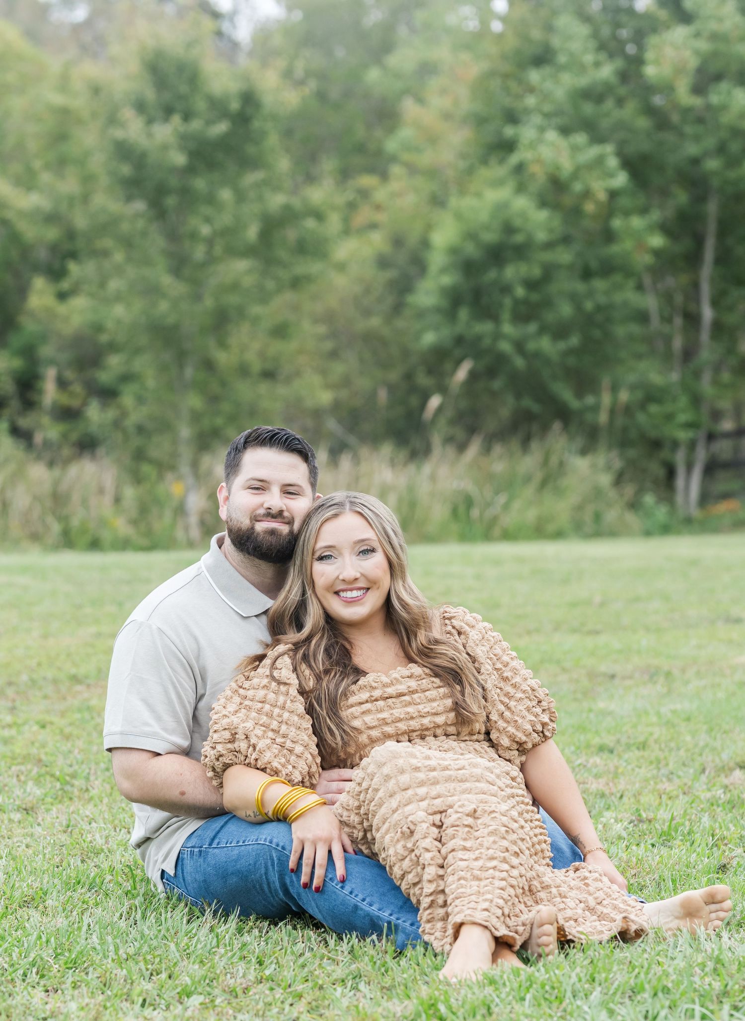 A couple relaxes on grass in an outdoor setting with the woman wearing a textured beige dress.