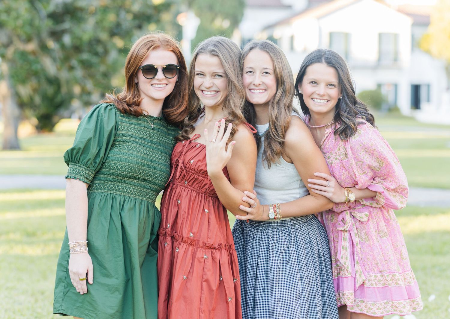 Four women in coordinating dresses stand together outdoors for a group photo in natural lighting.