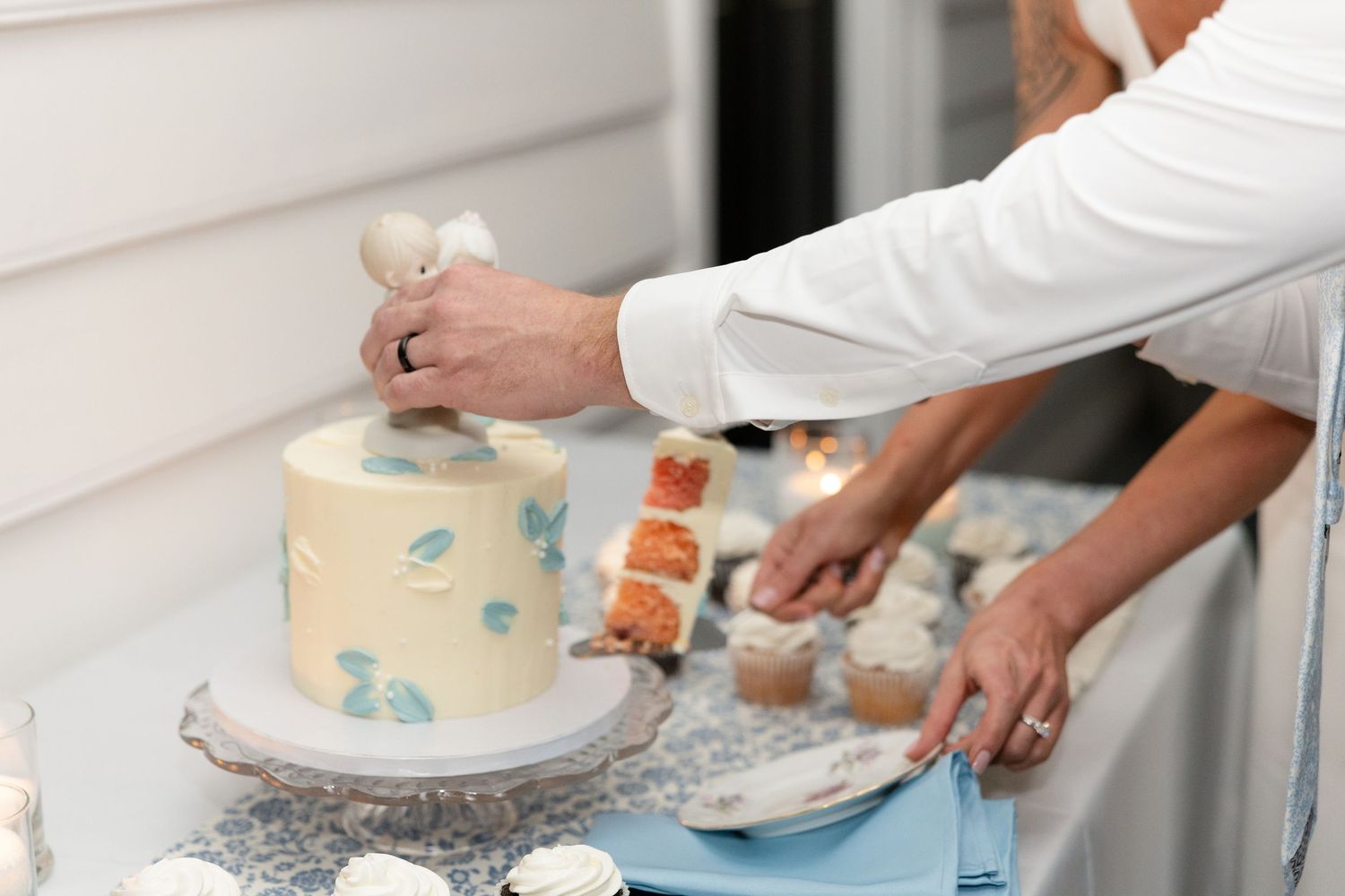 Bride and groom cutting a small white wedding cake with blue accents at an outdoor reception table.