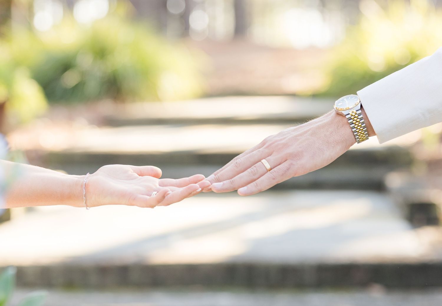 Close-up of bride and groom gently touching fingertips on stone steps in soft natural light.