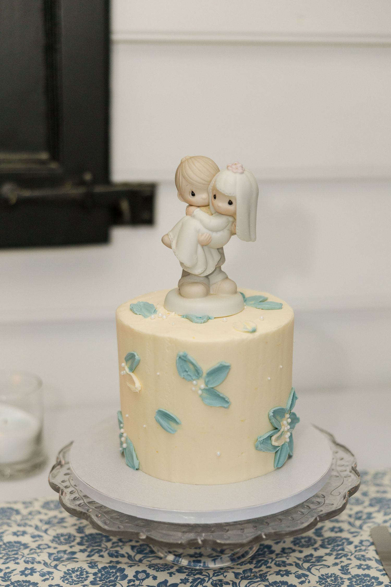 Small white wedding cake with blue floral details and classic Precious Moments bride and groom ceramic cake topper.