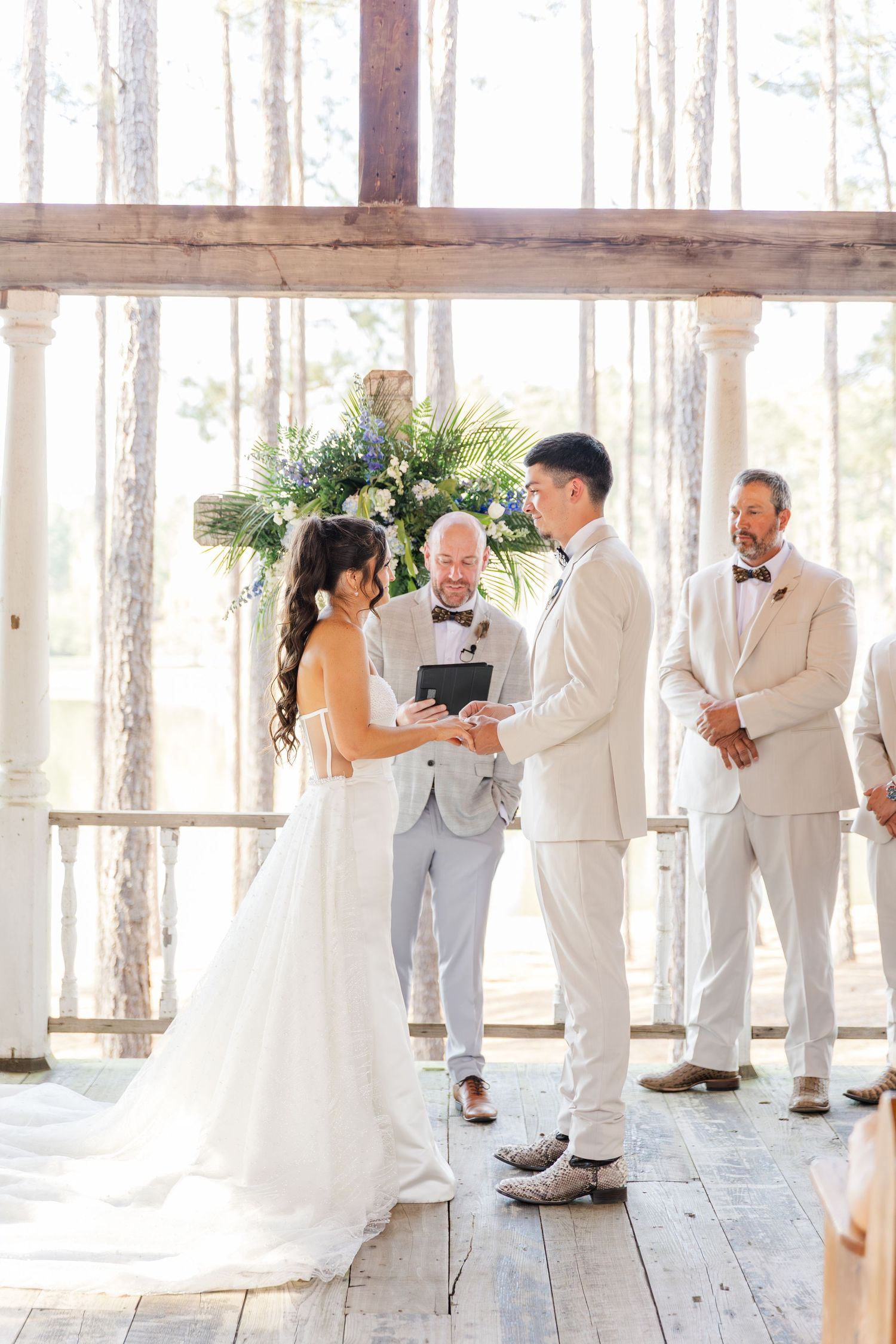 Bride and groom exchange vows at an outdoor rustic wedding ceremony with a floral arrangement backdrop.