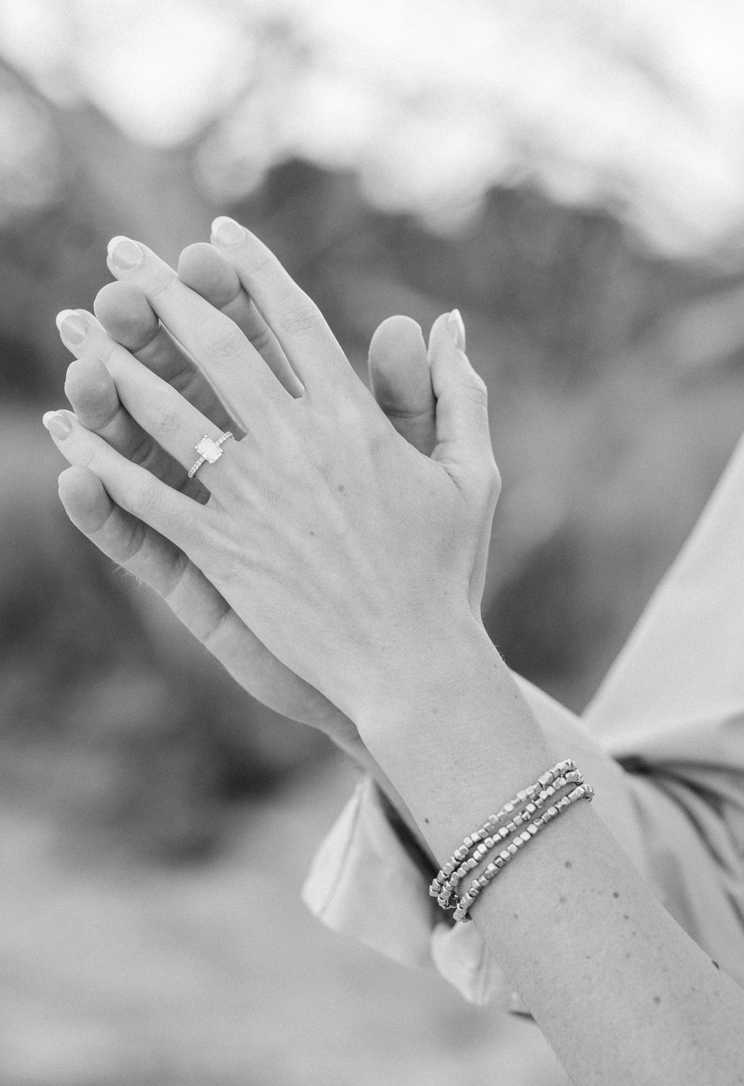 Black and white photo of hands clasped together wearing a wedding ring and elegant stacked bracelets.