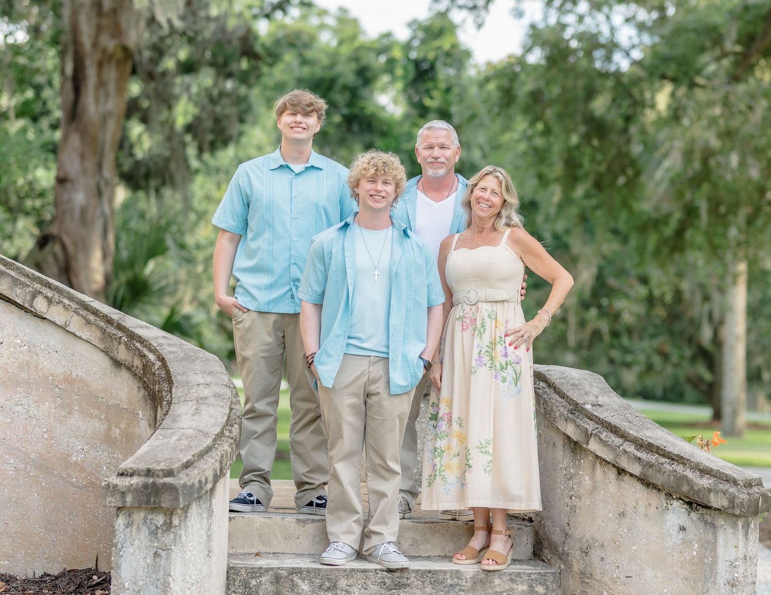 Family group poses on stone steps in an outdoor garden setting wearing coordinating light blue and white outfits.