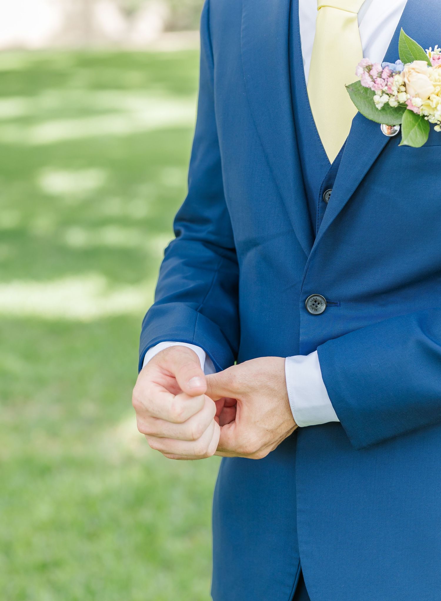 Detail shot of a navy blue suit jacket with yellow tie and boutonniere against a green lawn background.