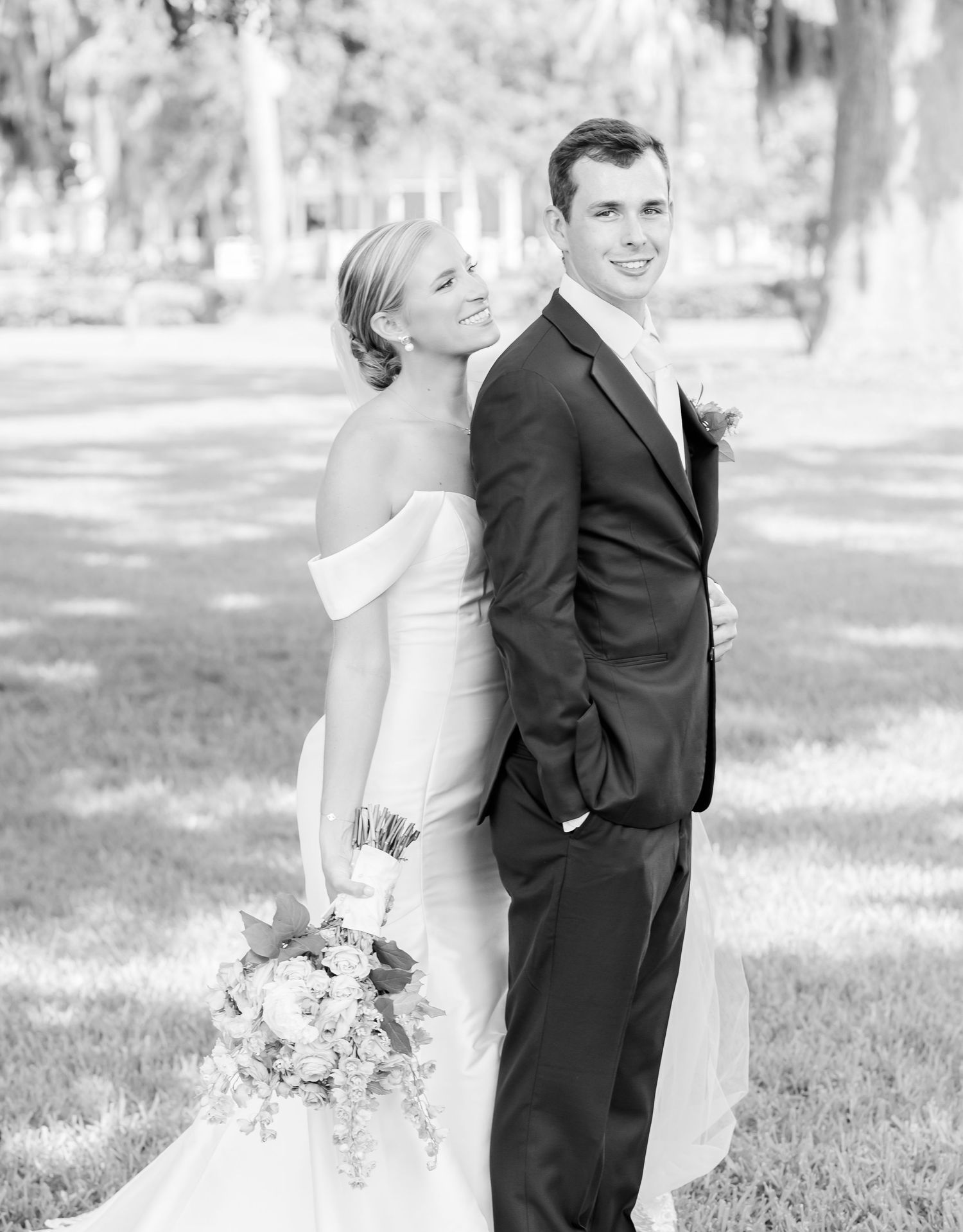 Elegant wedding couple pose back-to-back in a dreamy outdoor setting.