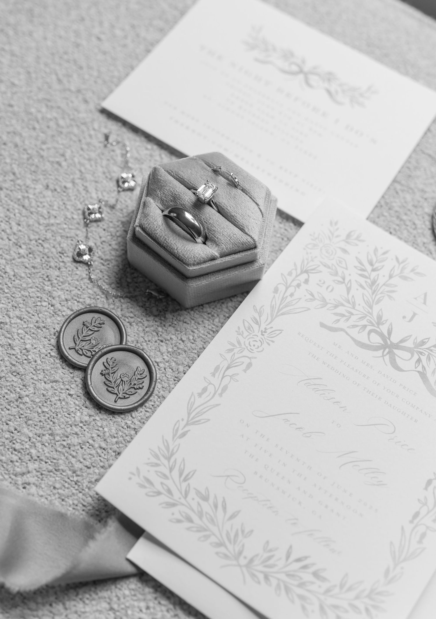 Wedding invitation suite with gray ring box, delicate floral details, and decorative coins on textured surface.