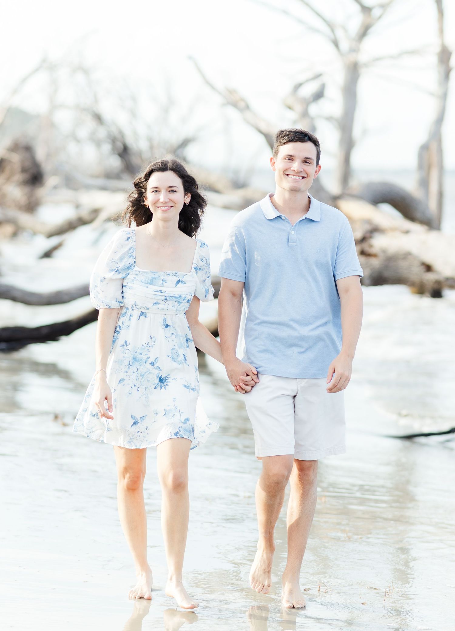 A playful couple walking hand in hand through shallow water at the beach.