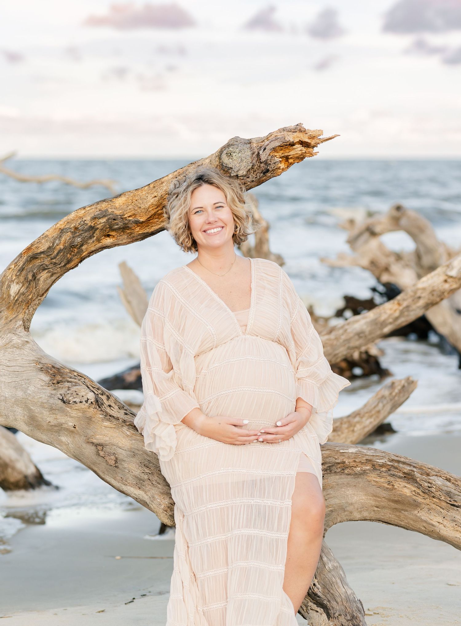 Maternity photo session on a beach with driftwood and soft peach dress.