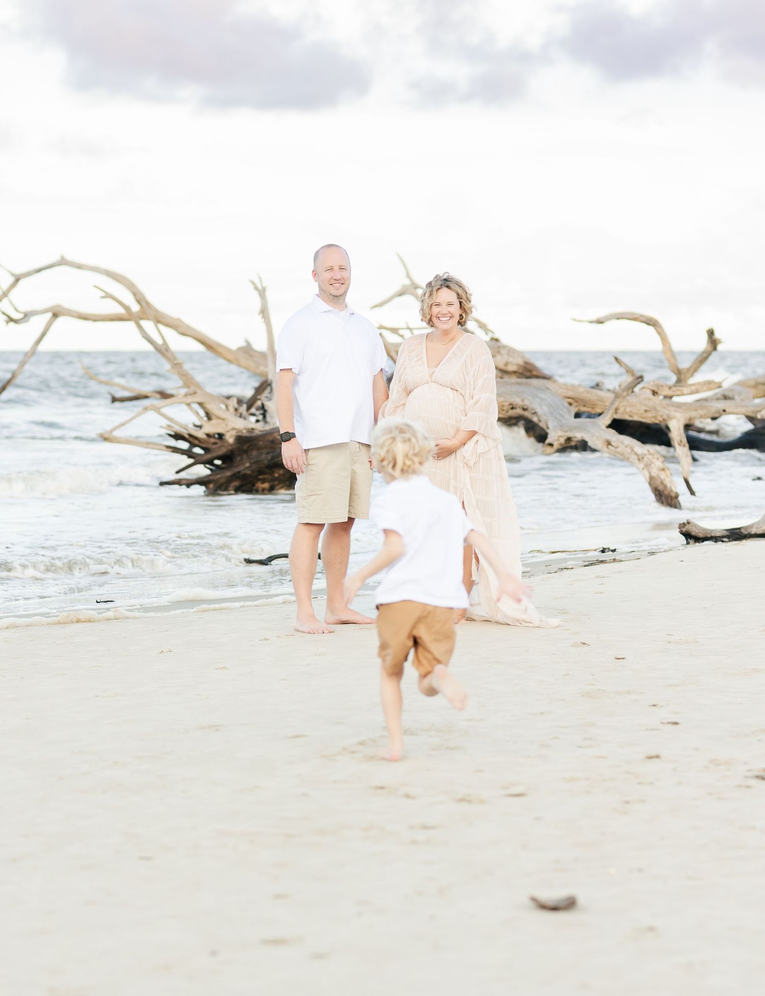 Playful family beach photography session with driftwood and ocean backdrop.