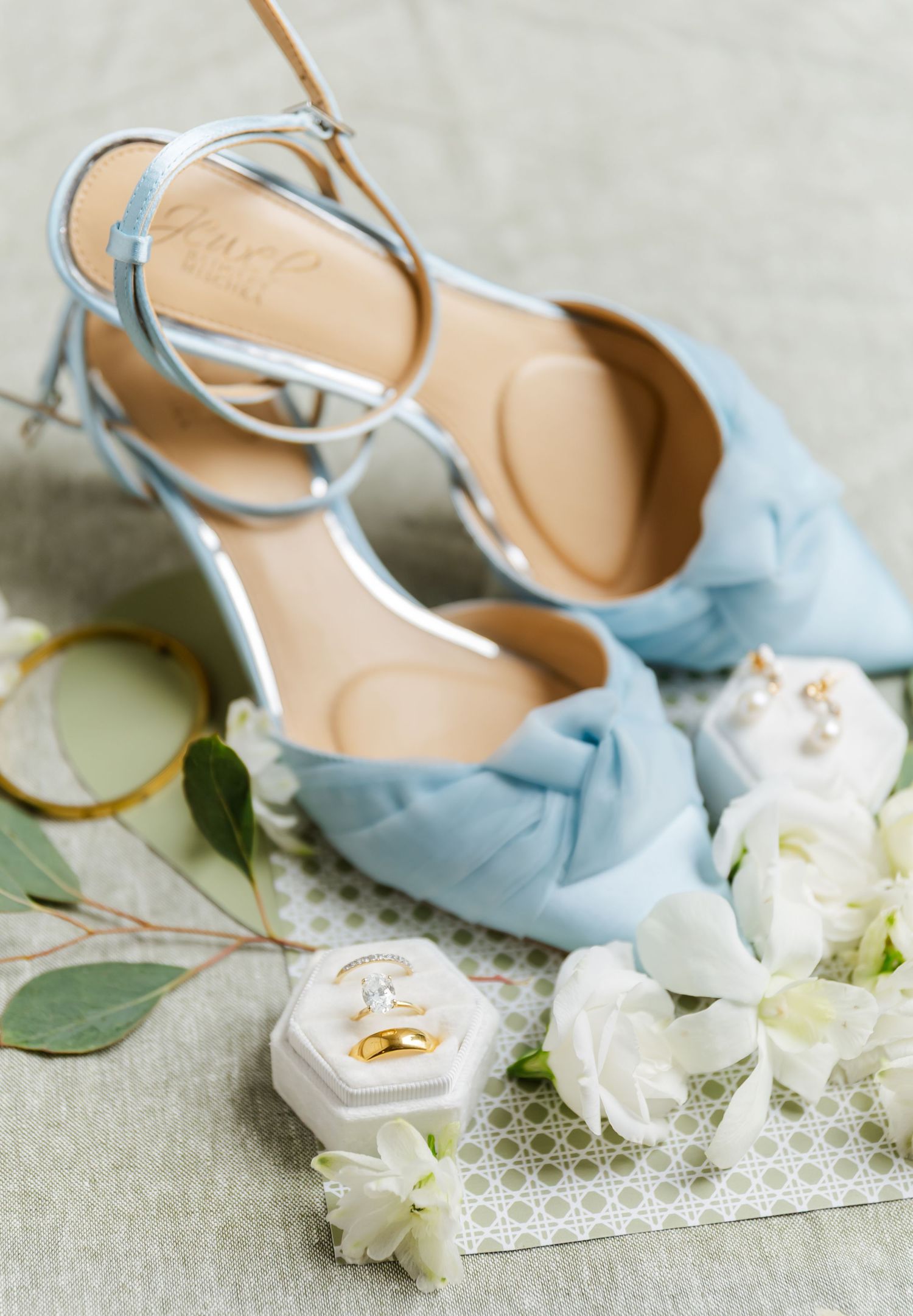 Light blue wedding shoes with white floral accessories arranged on delicate lace fabric.