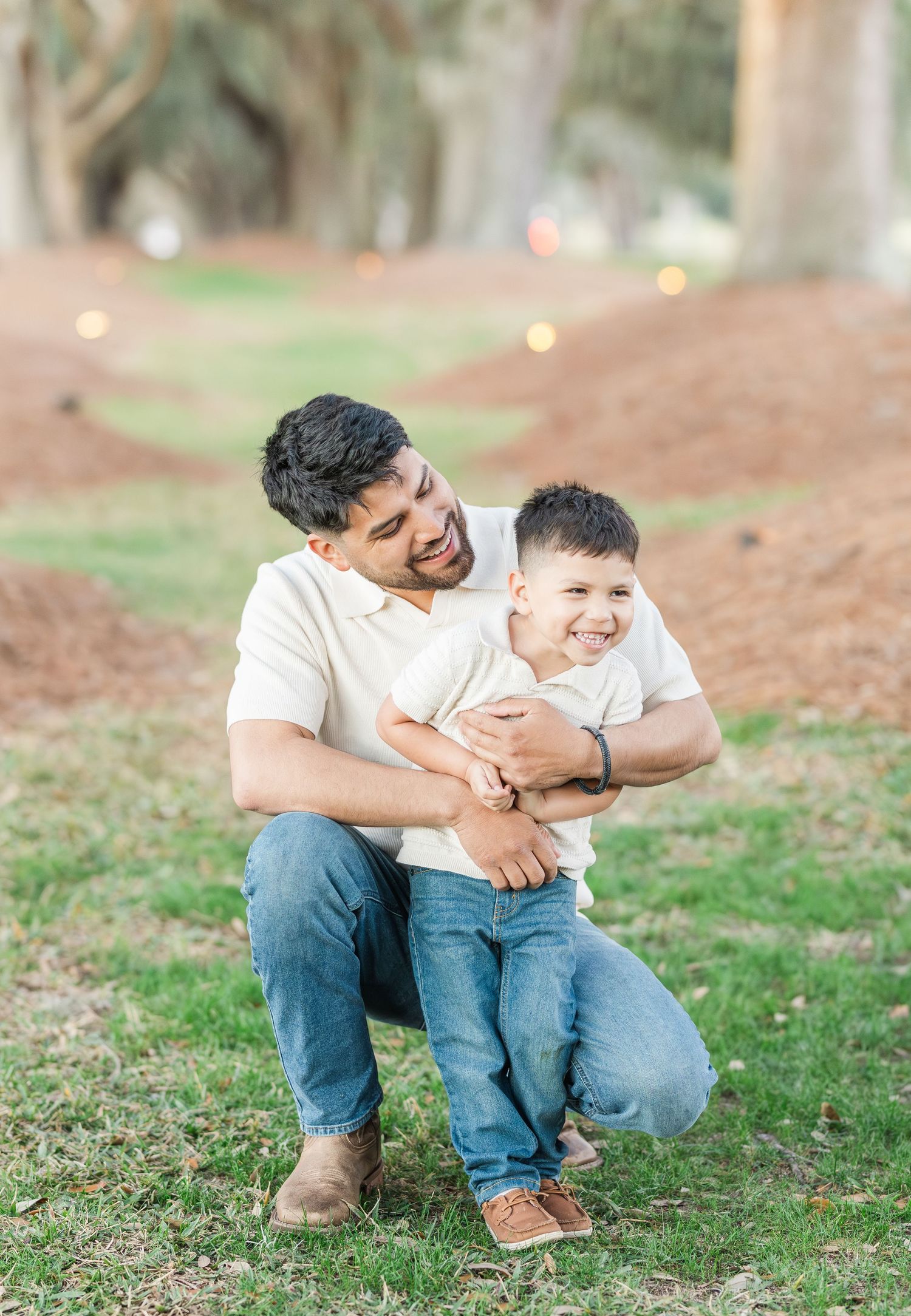 Family enjoying playful moments together on a grassy hillside during a casual outdoor photo session.