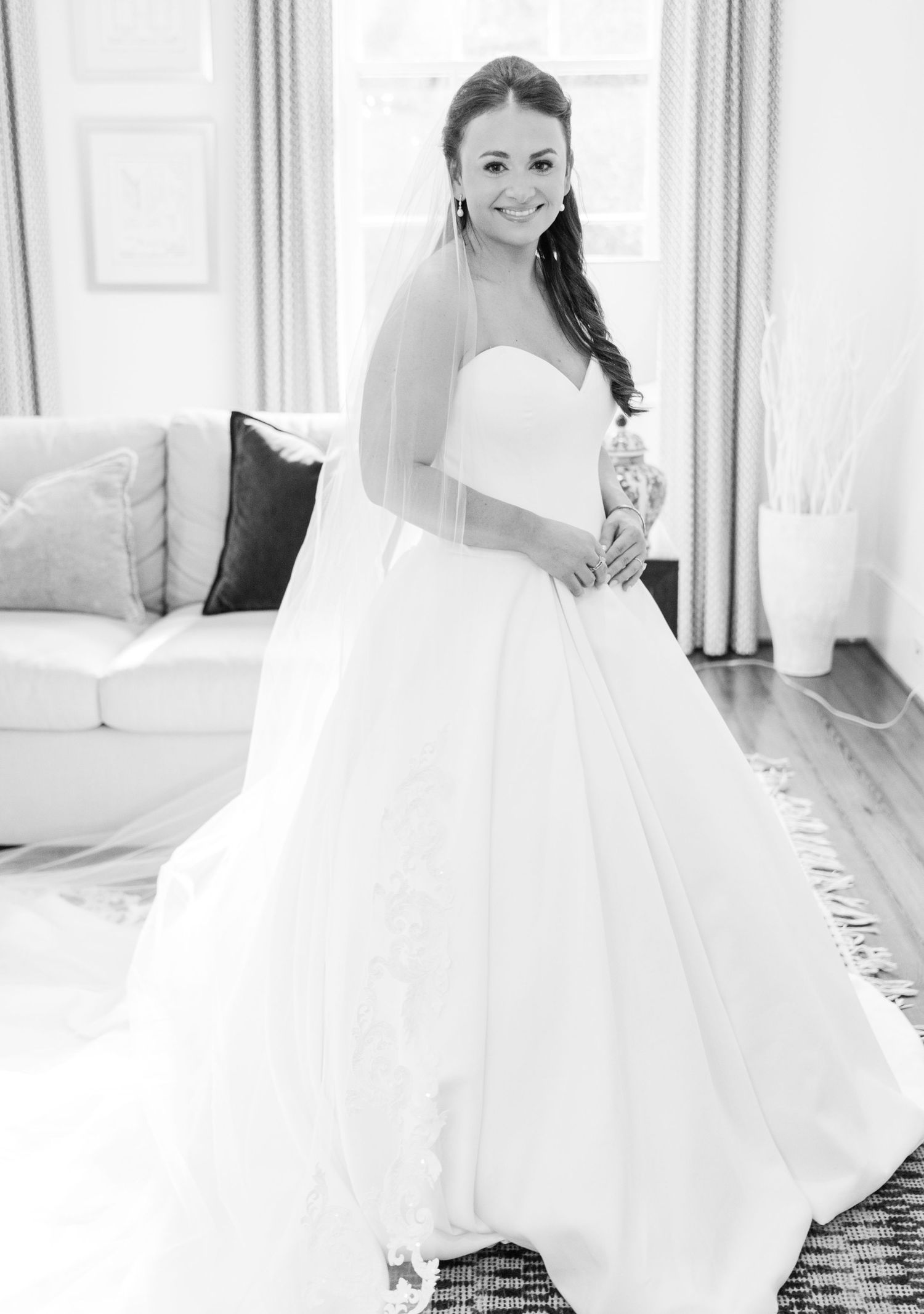 A bride in a flowing white wedding gown twirls and poses in a bright sunlit room.