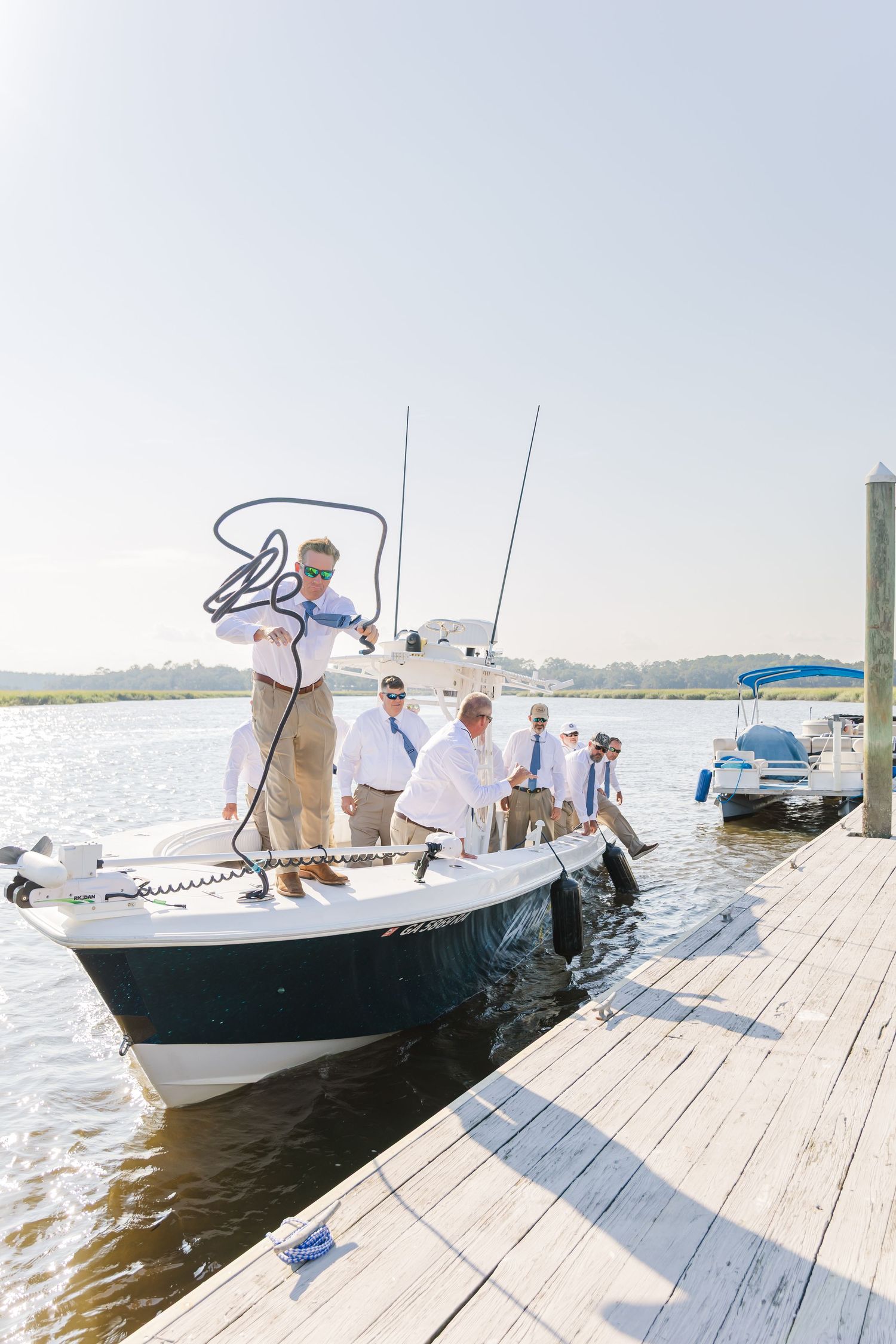 People in white shirts and khaki pants boarding a boat from a wooden dock on a sunny day.