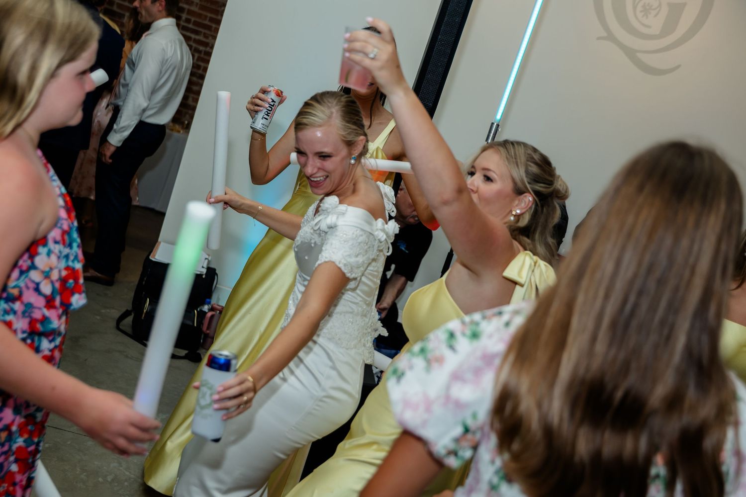 Wedding guests wave glowing LED foam sticks while dancing at a reception.