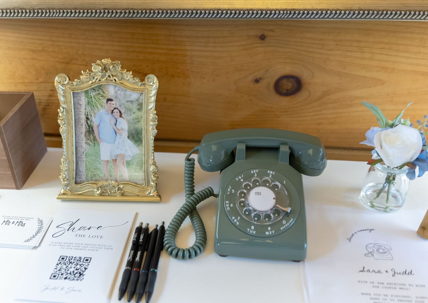 Vintage-inspired wedding decor display with antique telephone, ornate frames, and delicate paper goods on rustic wooden surface.