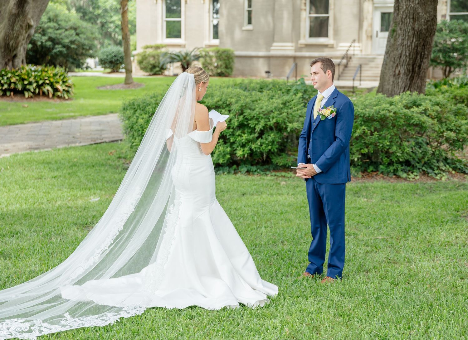 A couple in wedding attire shares a romantic first look moment in a lush garden setting.