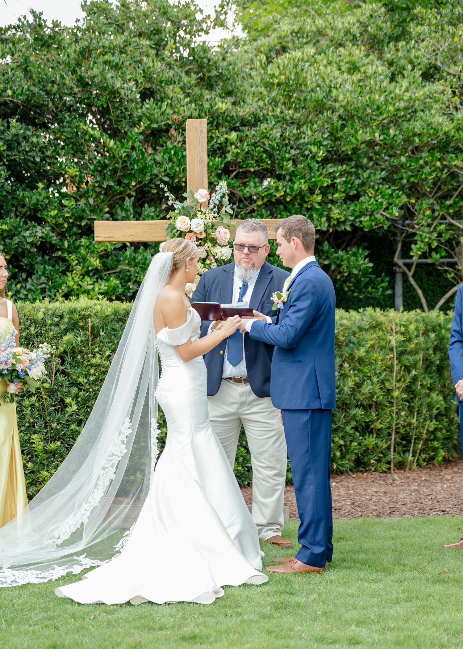 A wedding couple shares a romantic moment during their first dance on a lush green lawn surrounded by trees.