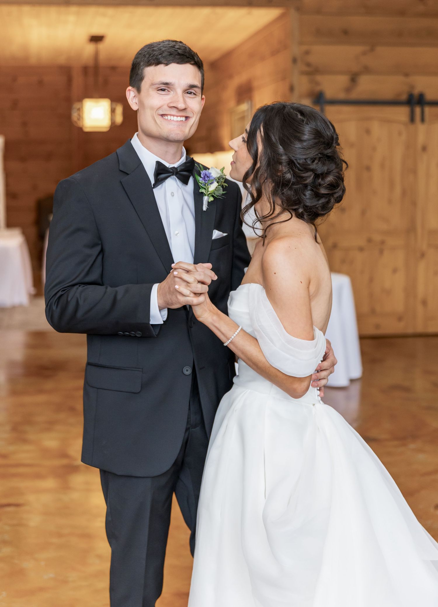 A couple shares their first dance in a rustic barn venue with wooden walls and warm lighting.