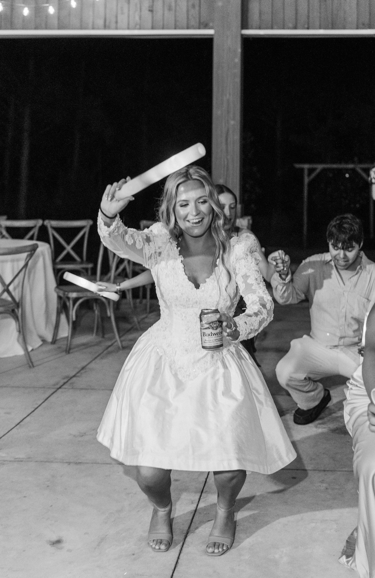 Black and white photo of bride in short reception dress dancing with baseball bat at wedding party.