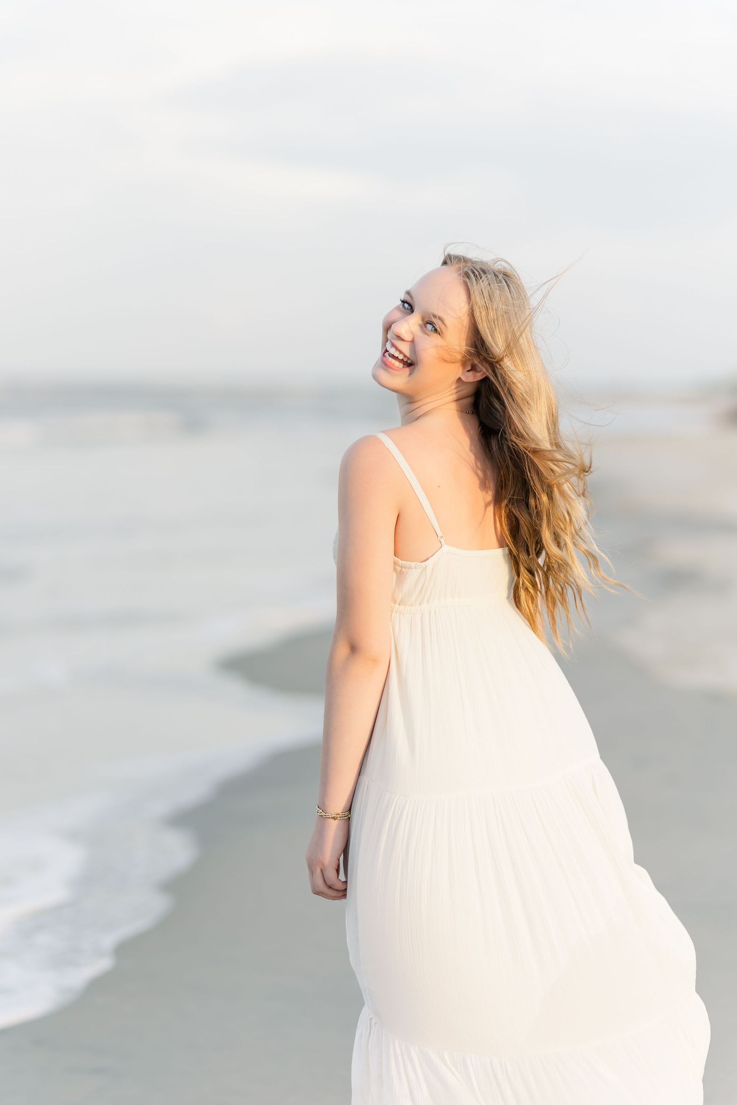 A joyful beach scene with flowing white dress catching the ocean breeze at sunset.