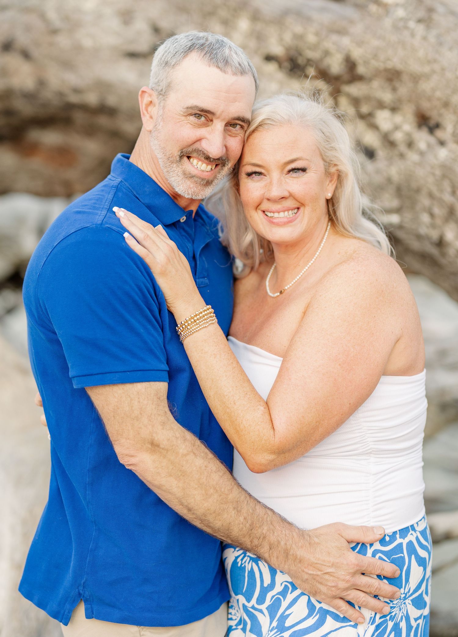 Happy couple embraces while posing together outdoors against a rocky natural backdrop.