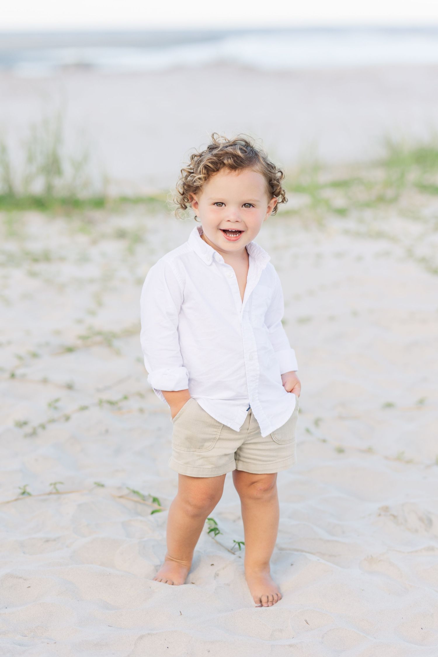 A small child wearing a white shirt and khaki shorts plays on a sandy beach in a series of candid shots.