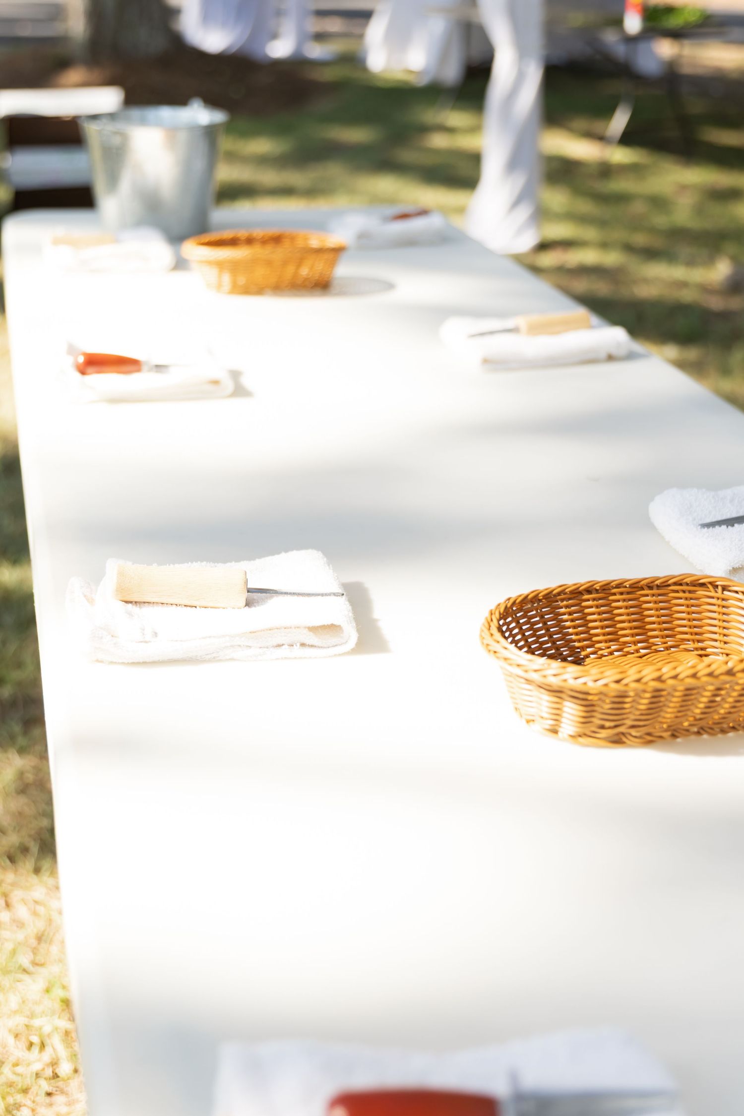 White tablecloths and wicker baskets are arranged on outdoor tables for an elegant garden dining setup.