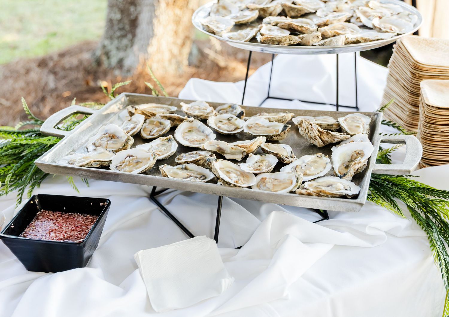 Fresh oysters displayed on tiered metal stands with cocktail sauce and garnishes.