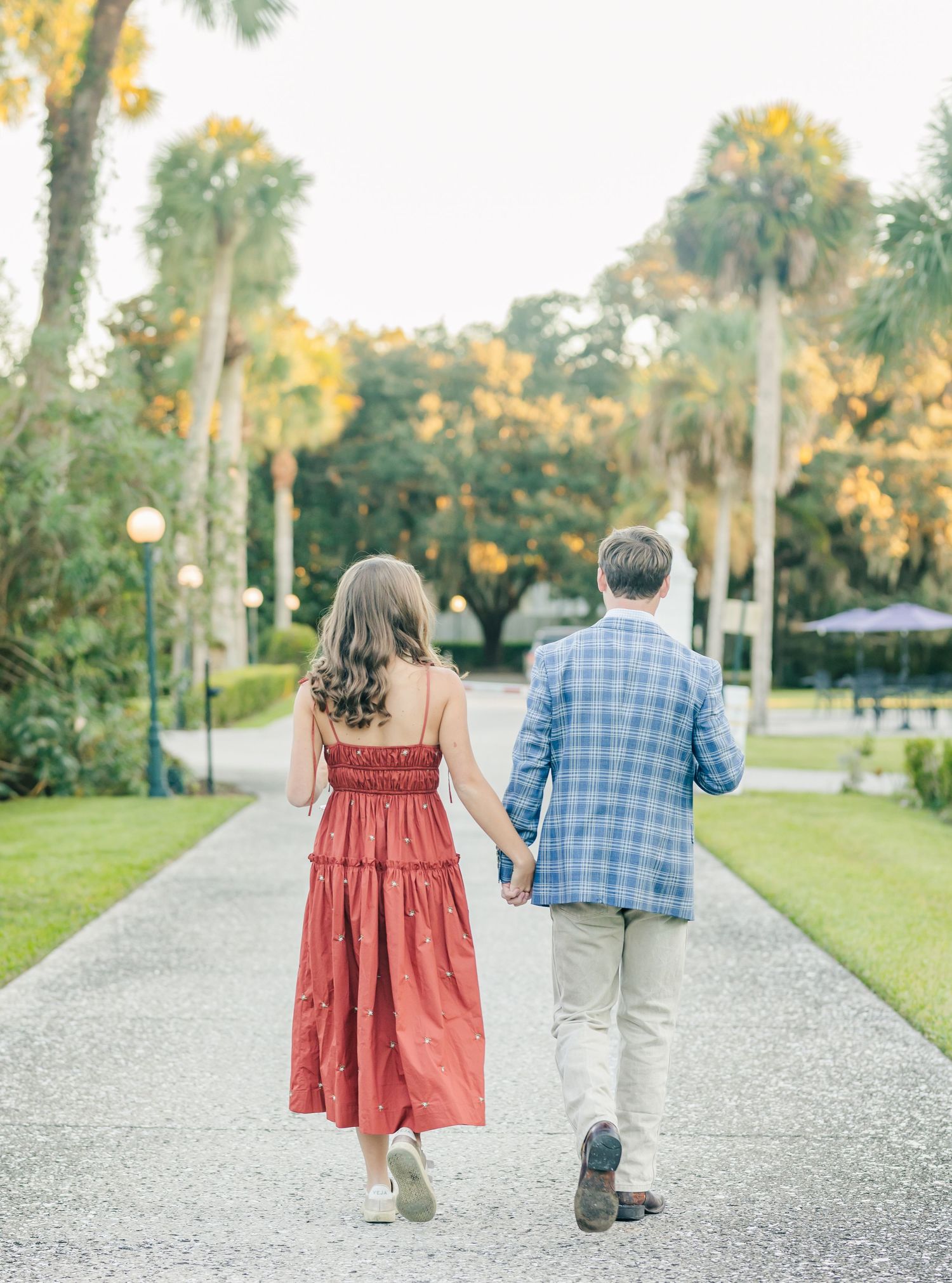 Couple walking hand in hand down a shell path surrounded by palm trees.