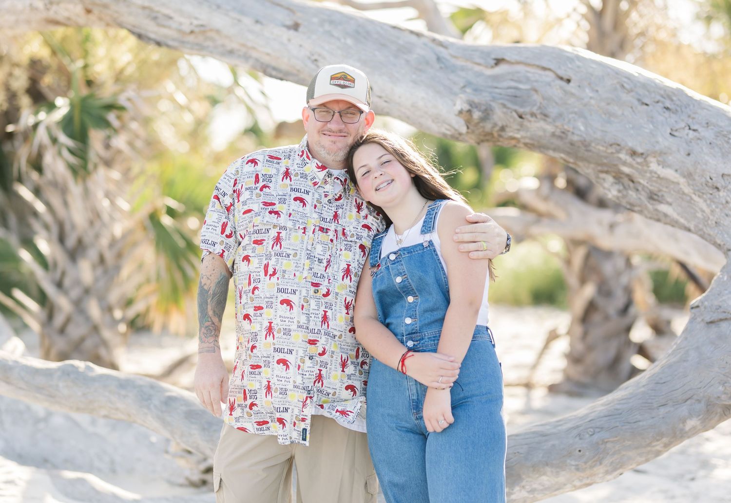 A couple poses together against a twisted tree branch on a sunny day at the beach.