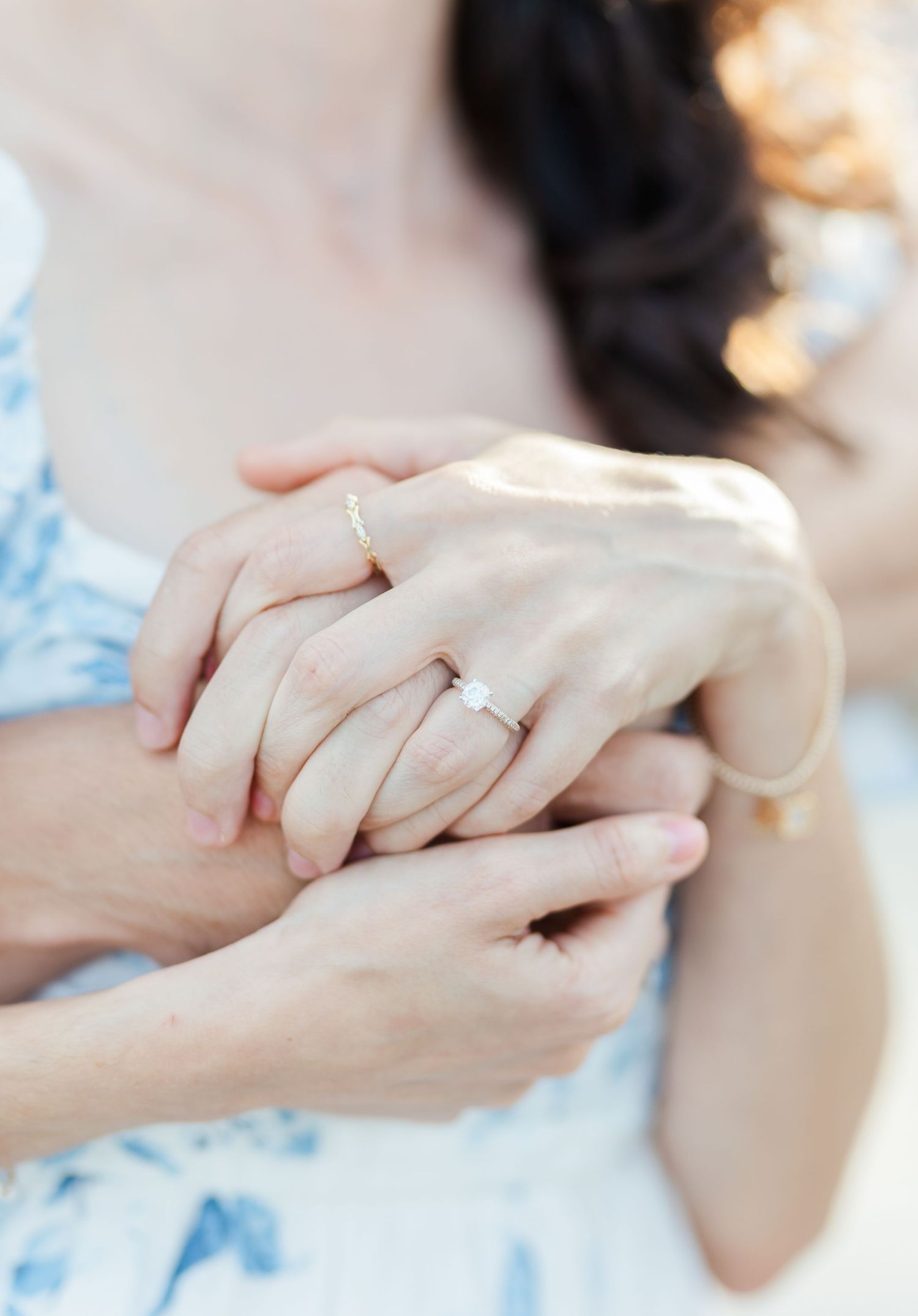 Close-up shot of hands with engagement rings being held tenderly against a light blue dress.