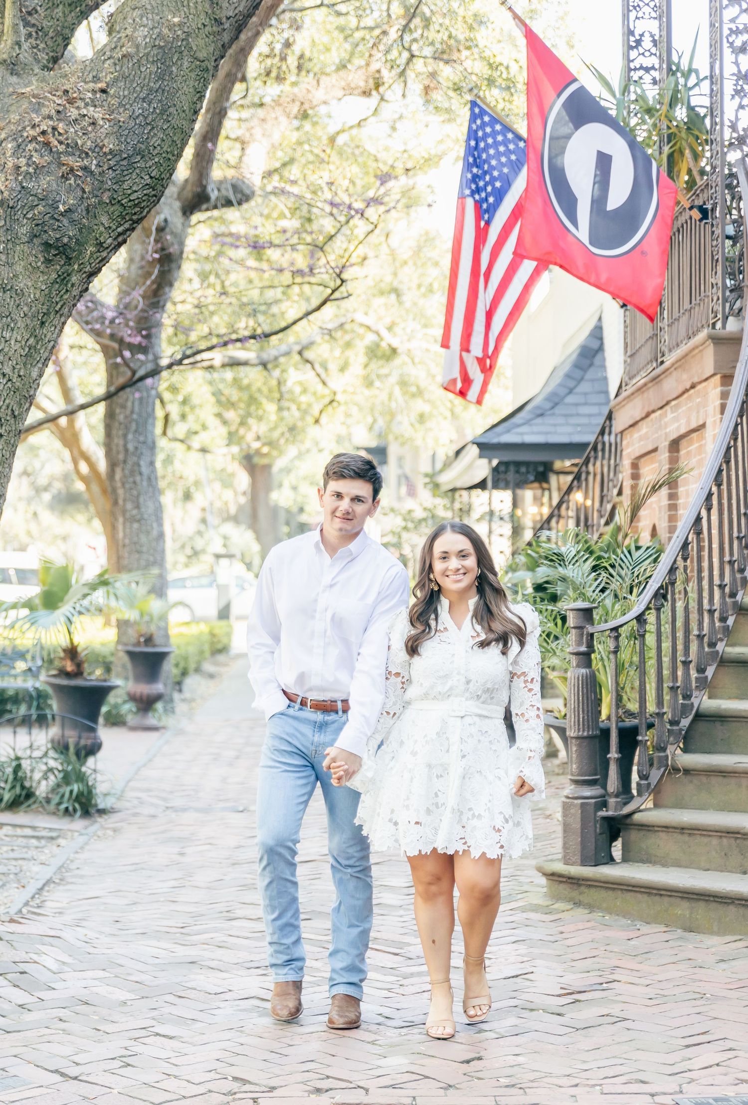 A couple strolls along a historic brick walkway with American and state flags decorating the street.