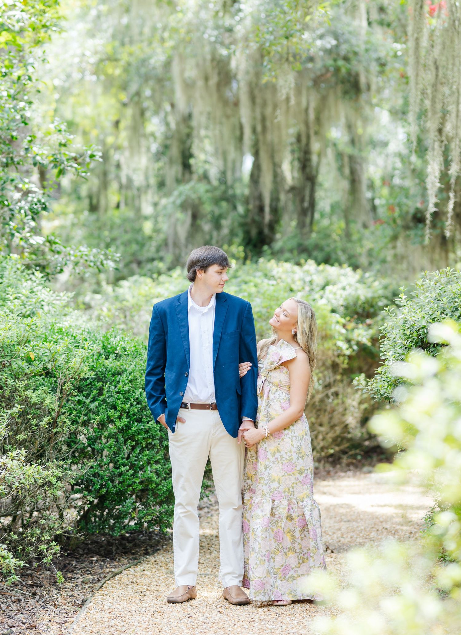 Romantic couple walking and laughing together on a moss-draped garden pathway.