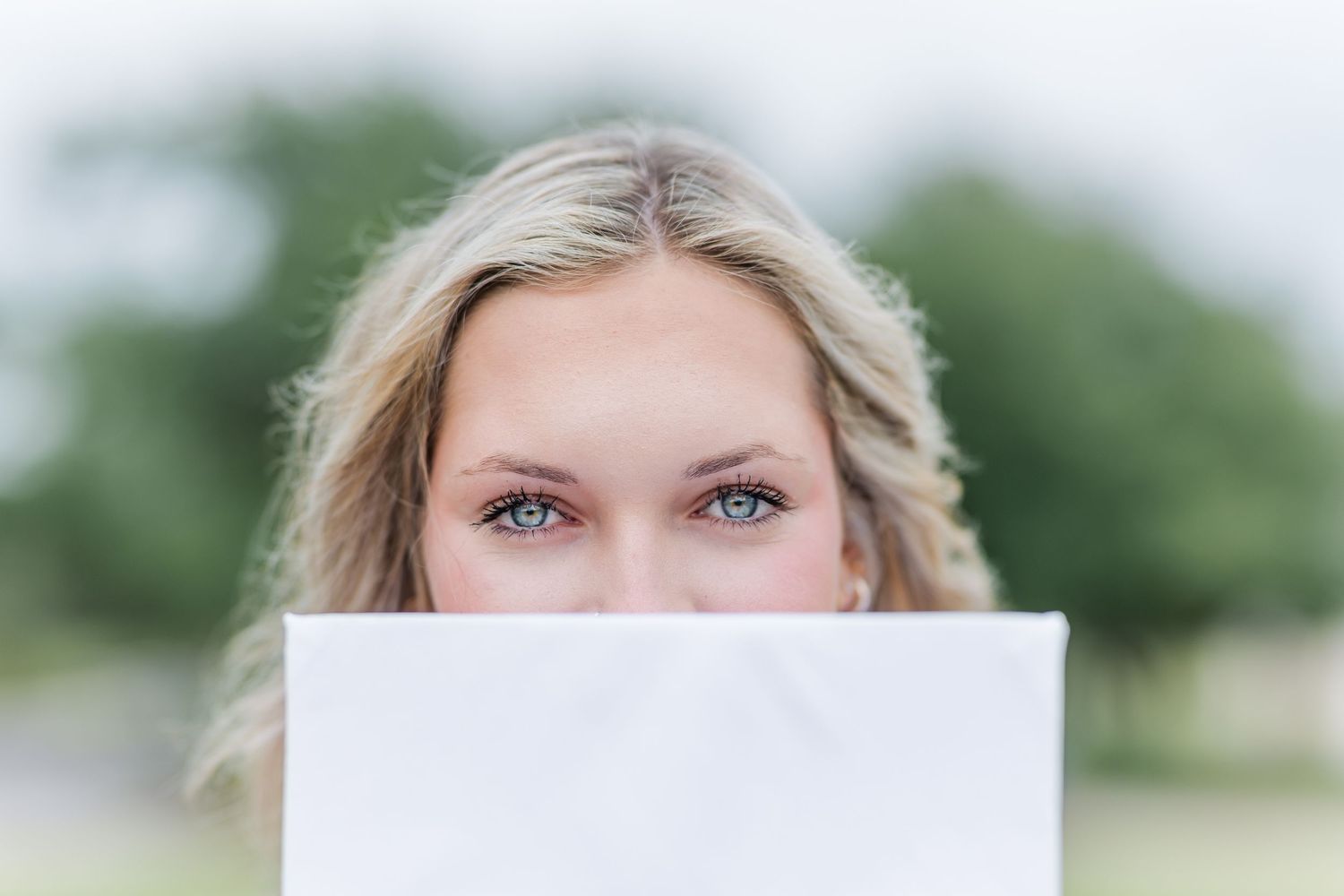 A graduation cap held up to partially cover someone's face in an artistic portrait.