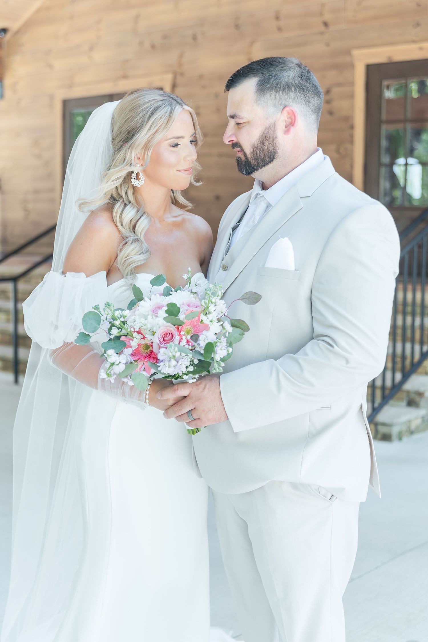 Intimate moment between wedding couple in white attire with romantic floral bouquet.