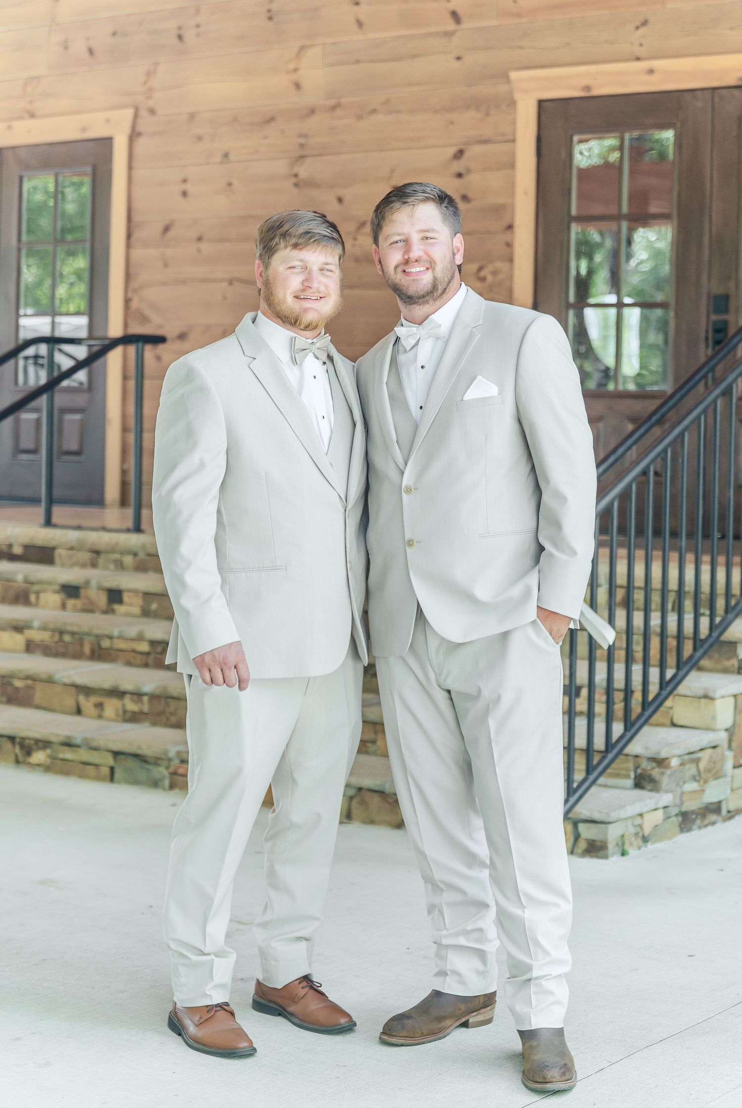 Two people in matching light beige suits smile together on rustic wooden porch.