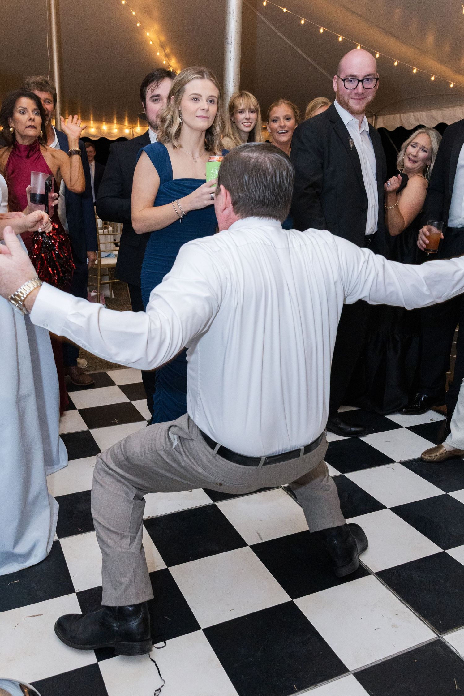 Wedding guest in white shirt does dramatic dance move on black and white checkered dance floor.