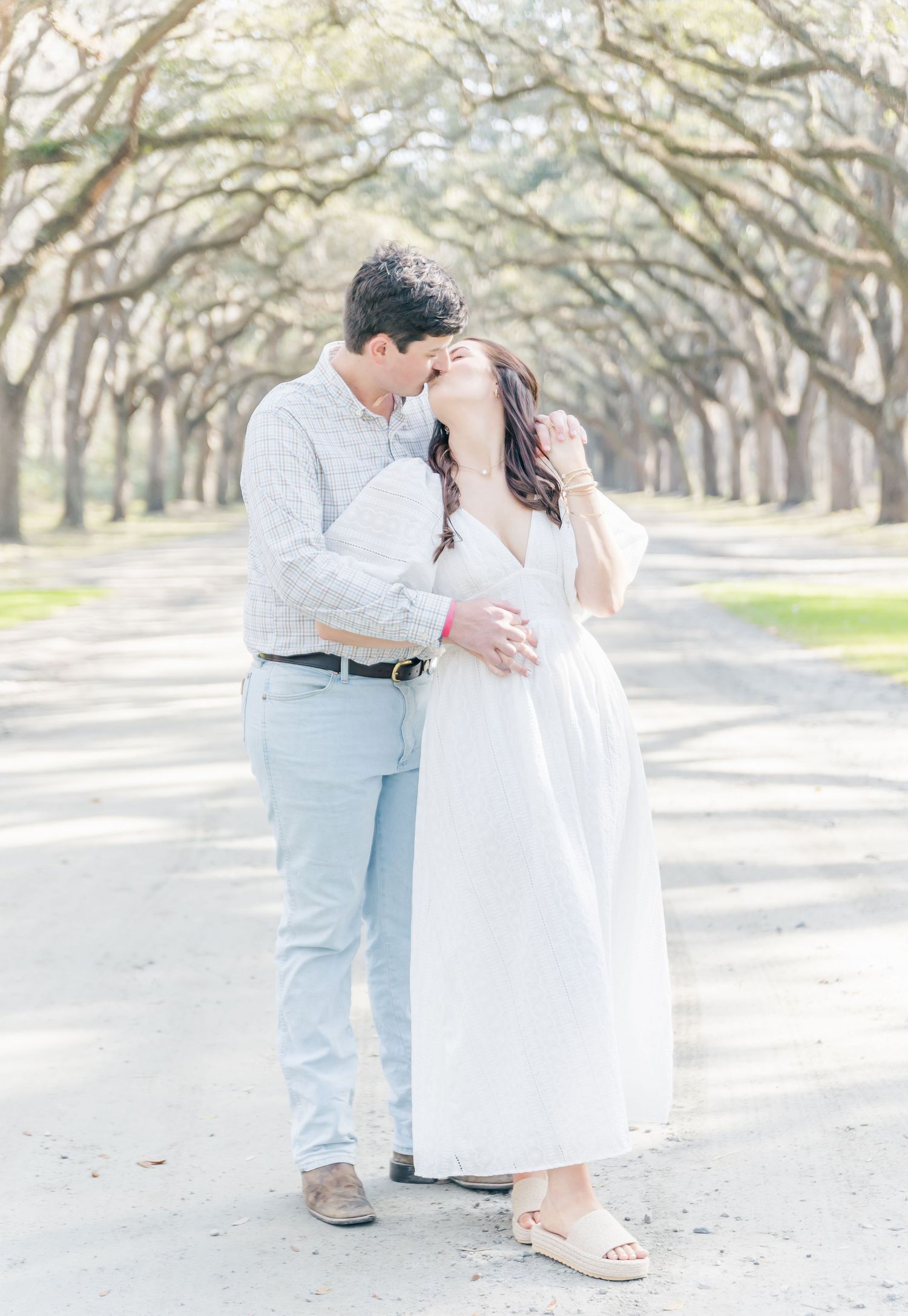 A romantic moment captured between a couple on a beautiful tree-lined avenue in soft lighting.