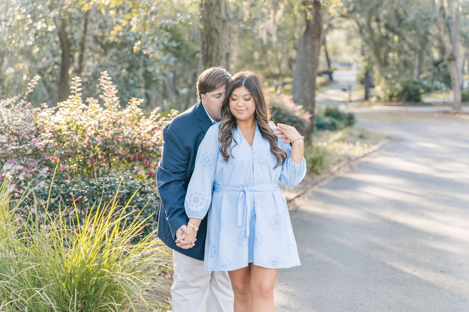 A couple in coordinating blue and white outfits share a romantic moment on a tree-lined path.