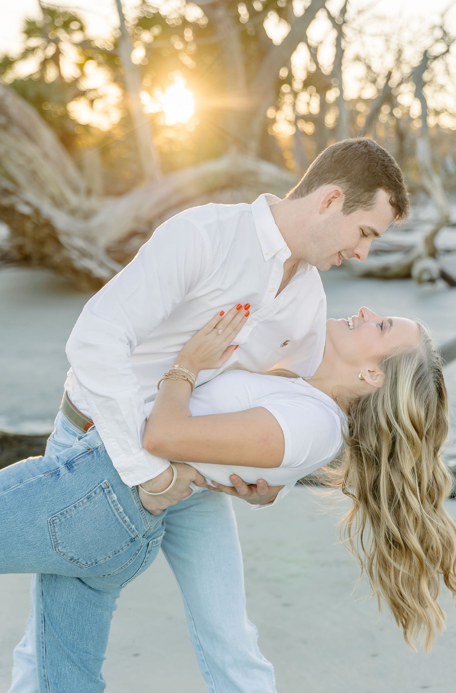 A couple performs a romantic dip pose on the beach at sunset.