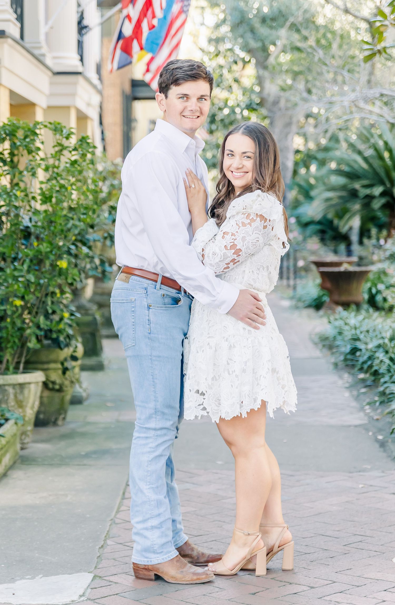 A couple shares a romantic moment on a Southern sidewalk with flags in the background.