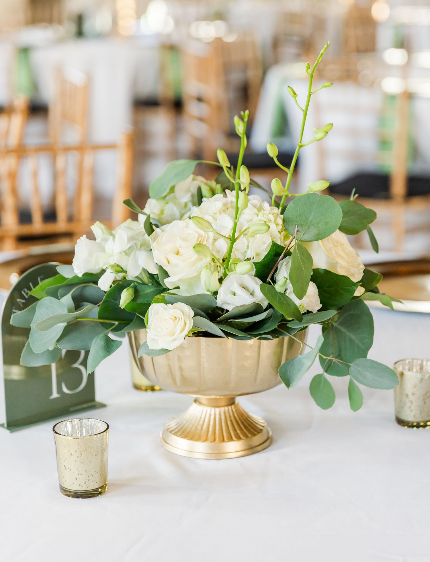 Elegant wedding table centerpieces featuring white flowers in gold vases with eucalyptus leaves.
